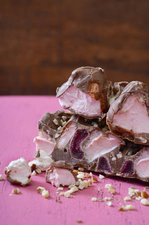 Closeup of chocolate candy with marshmallows, nuts and glace cherries on vintage pink wood table...