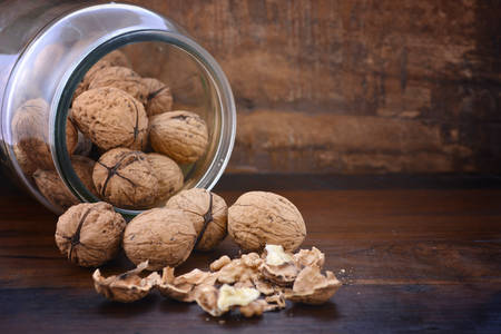 Fresh walnuts in shells falling out of glass jar on rustic dark wood table background.の写真素材