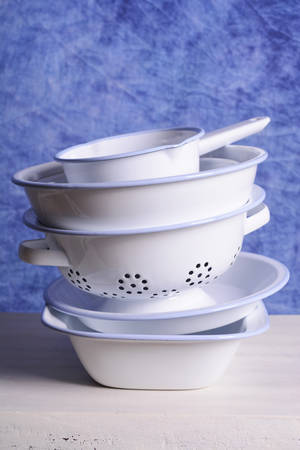 Stack of blue and white enamel bowls, including loaf pan, pie dish, colander strainer, mixing bowl and milk pan on white vintage wood table.の写真素材