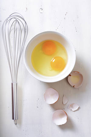 Cooking concept with broken eggs and metal whisk on vintage wood background.の写真素材