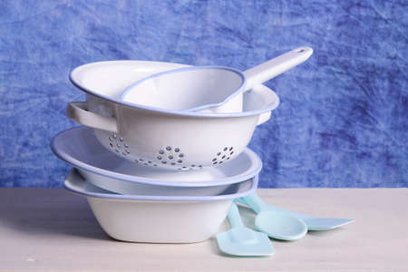 Stack of blue and white enamel bowls, including loaf pan, pie dish, colander strainer, mixing bowl and milk pan on white vintage wood table.の写真素材