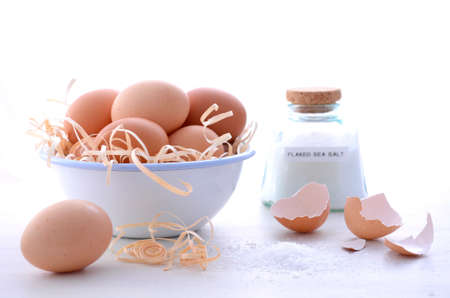 Farm fresh eggs in vintage bowl with broken egg shells and salt on vintage white wood table.の写真素材