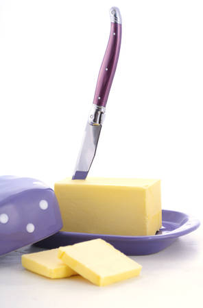 Butter in purple polka dot butter dish and knife on white wood table.の写真素材