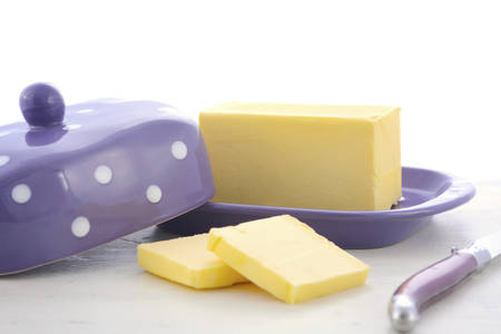 Butter in purple polka dot butter dish and knife on white wood table.の写真素材