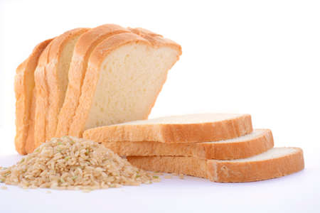 Loaf of sliced gluten-free rice sourdough bread with pile of raw brown rice on white table.