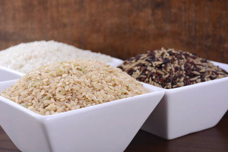 Square bowls of uncooked brown, white, and red and black rice on dark wood vintage background.の写真素材