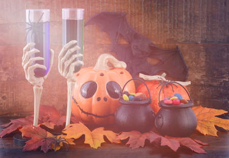 Happy Halloween Zombie Party decorations with green and blue drinks in skeleton hand glasses, pumpkins and candy on witches cauldrons on dark wood table background, with added retro vintage style filters and light stream lens flare.の写真素材