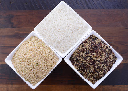Square bowls of uncooked brown, white, and red and black rice on dark wood vintage background, overhead view.の写真素材