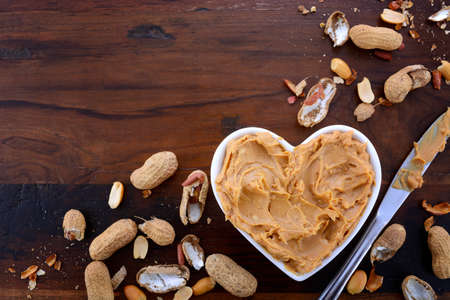 Crunchy peanut butter in white heart shape dish on dark wood vintage table.の写真素材