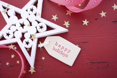 Christmas Happy background with white wood ornaments on red wood table, with closeup on Happy Holidays gift tag.の写真素材