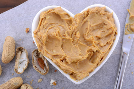 Crunchy peanut butter in white heart shape dish on dark wood vintage table.の写真素材