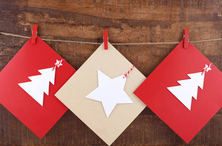Handmade Christmas greeting card using cutout shapes on natural kraft paper hanging from pegs on string line.の写真素材