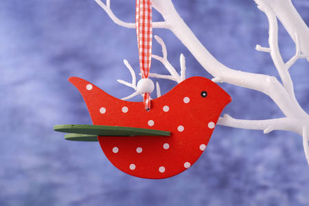 Modern Christmas decoration with red polka dot bird ornament hanging from white branch, against a blue background.の写真素材