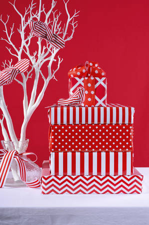 Stylish stack of festive Christmas red and white gifts with modern white tree branch and ornamental...