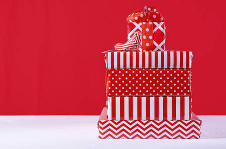 Stylish stack of festive Christmas red and white gifts on white table against a bright red background, and copy space for your text here.の写真素材