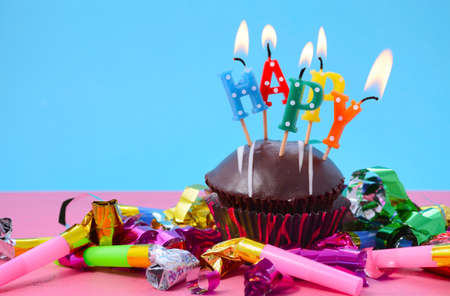 Chocolate Cupcake with Happy Candles and Party Decorations on bright pink and blue table.の写真素材
