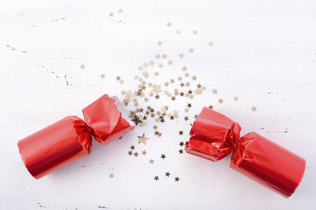 Festive surprise concept with opened red bon bon Christmas cracker and glitter stars on white wood table with copy space for your text here.の写真素材