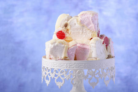 Festive white chocolate, cherry and nut candy on vintage style cake stand on white table and blue...