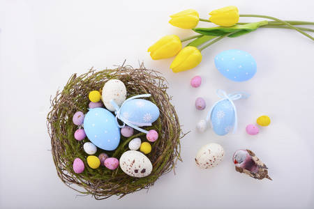 Happy Easter nest of candy, bird and polka dot eggs with yellow tulips and robin on white wood table...
