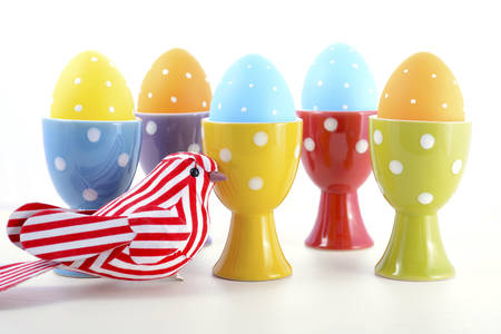 Happy Easter bright blue, yellow and orange polka dot Easter Eggs in egg cups with ornamental bird...