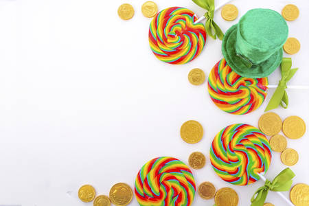 St Patricks Day Rainbow Lollipops with chocolate gold coins and leprechaun hat on white wood table flat layの写真素材