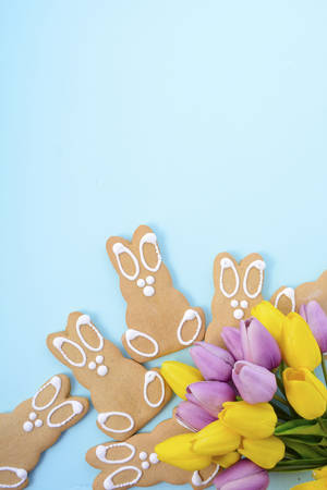 Happy Easter Gingerbread Cookie Bunnies with Spring tulips on pale blue wood table background.
