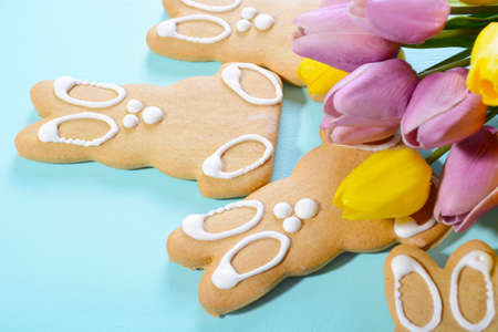 Happy Easter Gingerbread Cookie Bunnies with Spring tulips on pale blue wood table background, close up.の写真素材