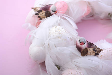 Pretty pink and white Easter door wall hanging wreath with eggs, feathers and robin bird decorations on a pink wood background, closeup.の写真素材