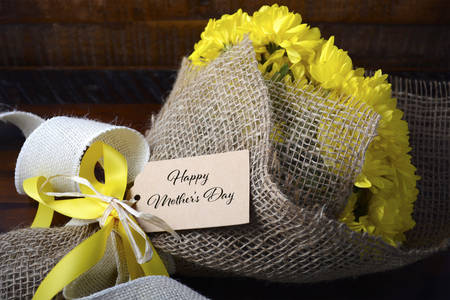 Modern theme yellow Bouquet of chrysanthemums wrapped in burlap on dark wood table for Mothers Day...