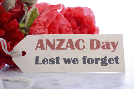 ANZAC Day, April 25, greeting with Lest We Forget and bunch of red silk poppies on white marble table, closeup.の写真素材