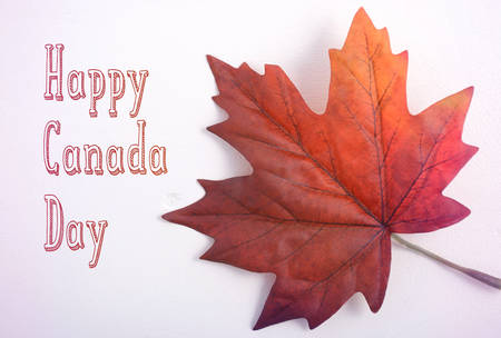 Happy Canada Day symbolic maple leaf on a white wood table with added light leak filters and on-trend handdrawn text.の写真素材