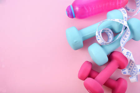 Health and fitness concept with pink and blue dumbells and accessories on a pink wood table, with copy space.の写真素材