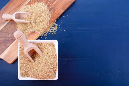 White grain quinoa with wooden scoops and chopping board on dark blue wood background, with copy space.の写真素材