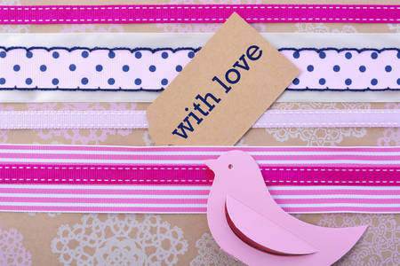 Modern holiday greeting background with close up of vintage gift wrapping with multiple ribbons and gift tag and paper bird on floral stenciled natural brown paper.の写真素材