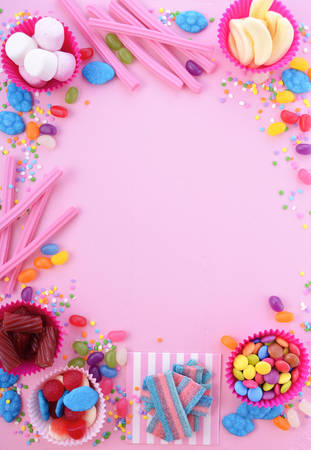 Background with decorated borders of bright colorful candy on pink wood table for Halloween trick of treat or childrens birthday party favors.の写真素材