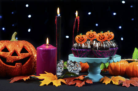 Halloween party table with chocolate cupcakes, spiders, pumpkins and candles against a black background with sparkling fairy lights.の写真素材
