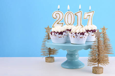 Happy New Year cupcakes with 2017 candles in a blue, gold and white winter theme setting background, on cakestand with gold Christmas trees, with copyspace.の写真素材