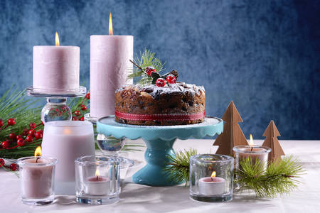 Festive holiday table with English style Christmas fruit cake with glamorous table setting with pink candles and blue background, with copy space. の写真素材