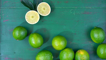 Limes on rustic dark green wood table overhead, with copy space.