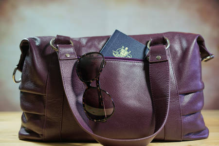 Travel concept with sunglasses and passport in purple carry bag.の写真素材