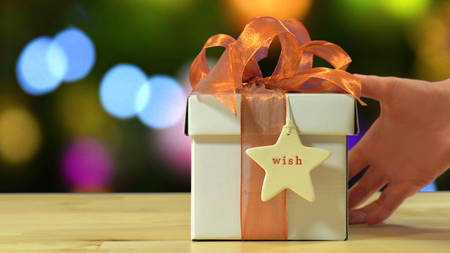 Modern gold, copper and white wrapped gift in front of bokeh lights of Christmas tree.