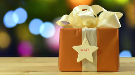 Modern gold, copper and white wrapped gift in front of bokeh lights of Christmas tree.の写真素材