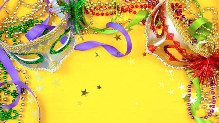 Mardi Gras overhead background with colorful masks and beads on rustic yellow wood background, with copy space.