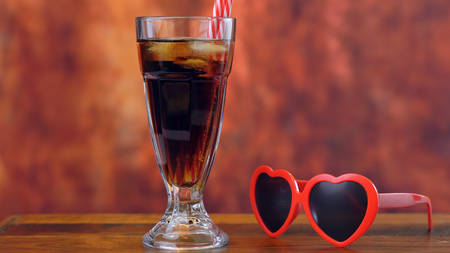 Pouring cola soft drink on ice in tall cafe glasses against a rustic wood background.の写真素材