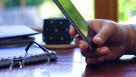 Man using smart phone closeup, at desk backlit by sunshine with reflections through window.