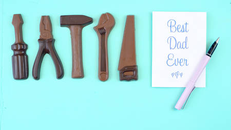 Happy Fathers Day overhead of chocolate tool set with Best Dad Ever greeting card on pale blue aqua table.の写真素材