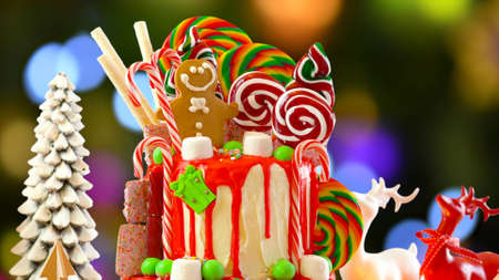 On trend festive candyland Christmas drip cake against festive Christmas tree bokeh lights background.の写真素材