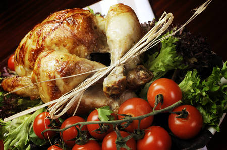 Platter of delicious roast chicken turkey with salad greens and red tomatoes on the vine for a succulent, delicious Christmas or Thanksgiving lunch or dinner meal - angle close up.の写真素材