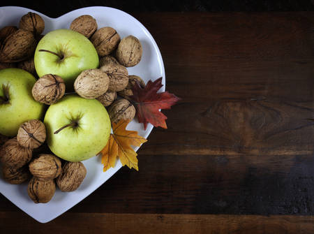 Happy Thanksgiving Autumn Fall harvest fruits with green apples and walnut nuts in white heart shape plate on dark recycled wood background, with copy space.の写真素材
