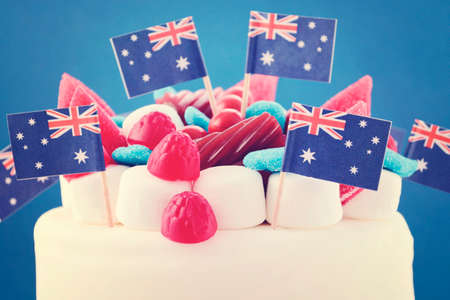 Happy Australia Day celebration cake with flags, marshmallow and candy decorations on a red cake stand on a white table against a blueの写真素材
